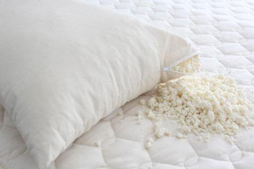 A white pillow with a zipper is partially open, revealing a pile of small, crumbled white material spilling out onto a quilted mattress below. The surface of the mattress is also white, creating a clean and soft appearance that truly makes this the best pillow for any bedroom.