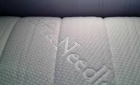 Close-up image of a white, textured mattress with "Tuft & Needle" elegantly embossed onto its surface. The fabric boasts a dotted pattern for added texture.