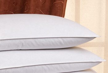 Two white pillows are stacked on top of each other in front of a brown and beige curtain background. The pillows appear fluffy and clean, much like those praised in many Hilton Pillow Reviews, suggesting they are ready for use or display.