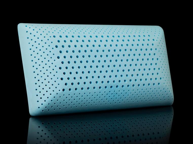 A teal, rectangular foam pillow by Malouf with evenly distributed ventilation holes sits against a black background, reflecting softly on a smooth surface.
