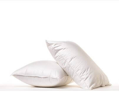 Two white Parachute pillows in a clean, minimalistic setting. One pillow is lying flat while the other is propped up against it, both showcasing a soft and fluffy texture against a neutral white background.