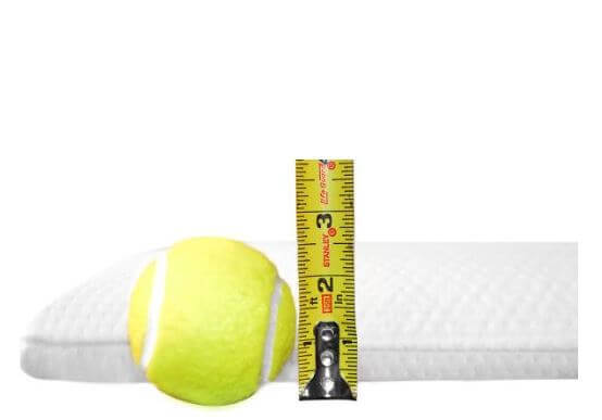 A yellow tennis ball and a measuring tape stand next to a white textured cushion, ideal for a stomach sleeper pillow. The measuring tape shows a height measurement slightly over 3 inches.