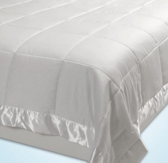 A close-up view of a bed with a neatly spread light gray comforter featuring a quilted pattern. The down alternative comforter has a satin trim along the edges, and the bed appears to be made on a plain light-colored surface.