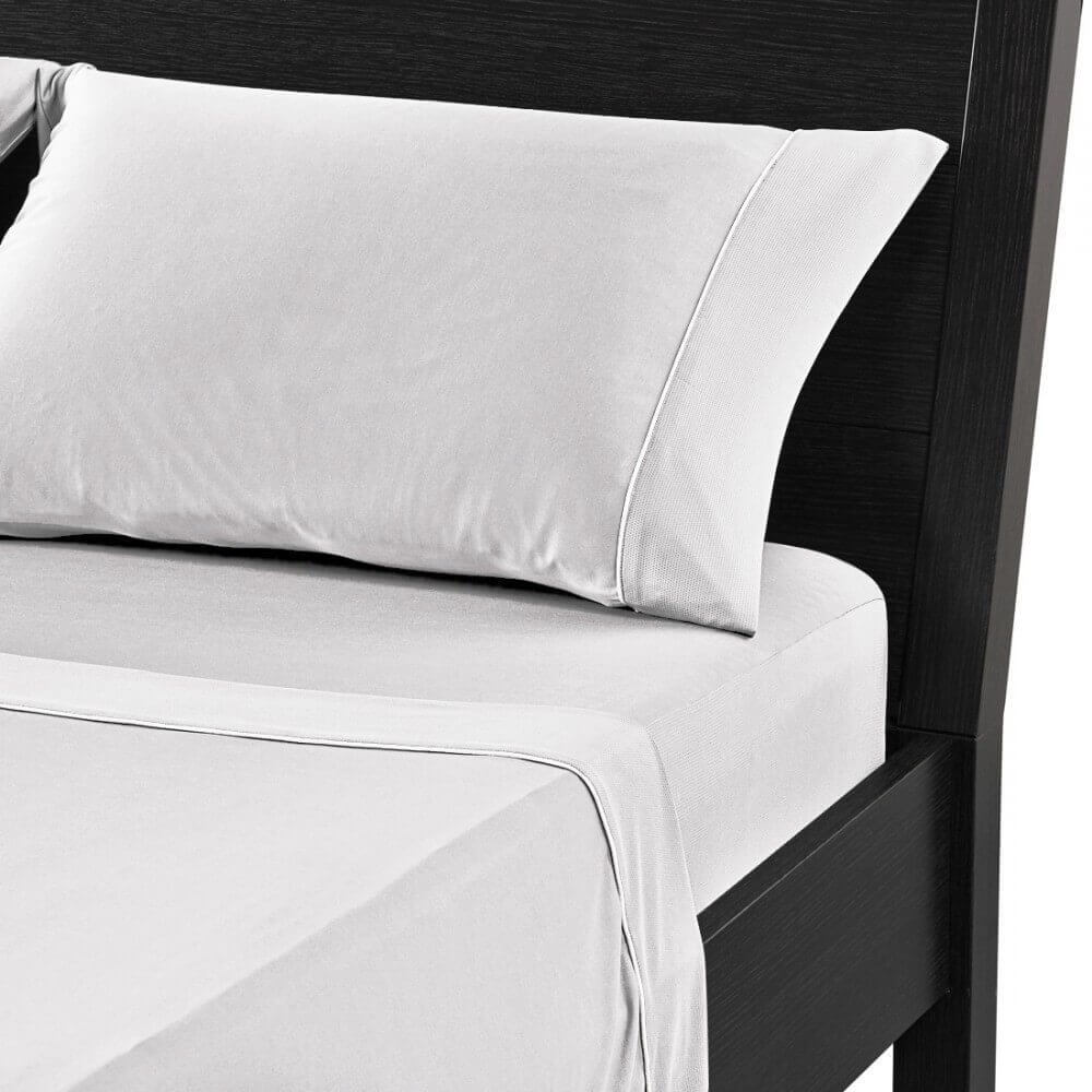 A neatly made bed with a black wooden frame, adorned with gray bedgear sheets and pillowcases. The photo focuses on the top corner of the bed, showcasing a single pillow and part of the fitted sheet and duvet.