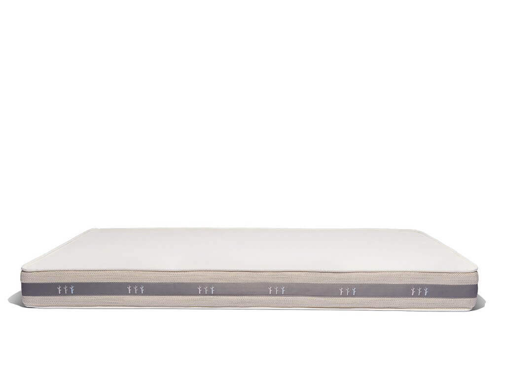 A side view of a rectangular crib mattress with a light gray and white fabric exterior. The sides feature small, repeating motifs of three figures. The mattress is placed against a plain white background.