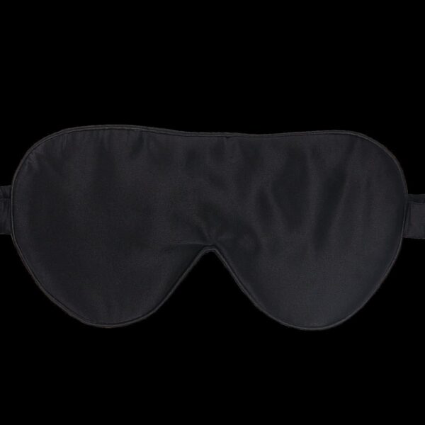 A black sleep mask with an elastic strap, designed to cover the eyes completely, lies against a plain black background. The mask has a smooth, slightly glossy fabric finish.
