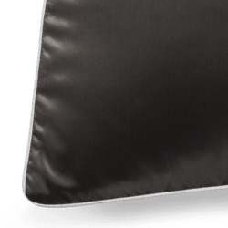 A close-up of a black silk pillowcase with white piping along the edges. The smooth texture of the pillowcase is highlighted by the light, creating a subtle sheen. Only the corner and a small portion of the front of the pillowcase are visible.