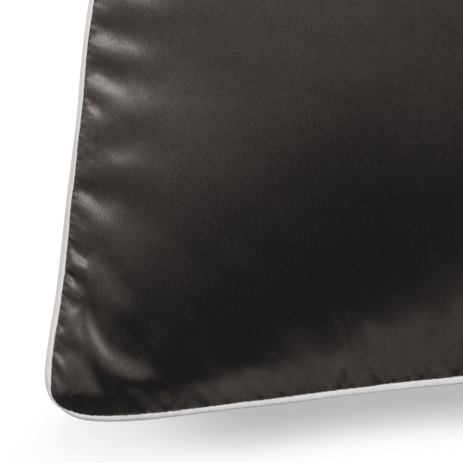A close-up shot of a black Silk Pillowcase with elegant white piping along its edges. The fabric boasts a smooth and glossy texture, and the seam along the piping is clearly visible. The lighting accentuates the luxurious quality of the pillowcase's material.