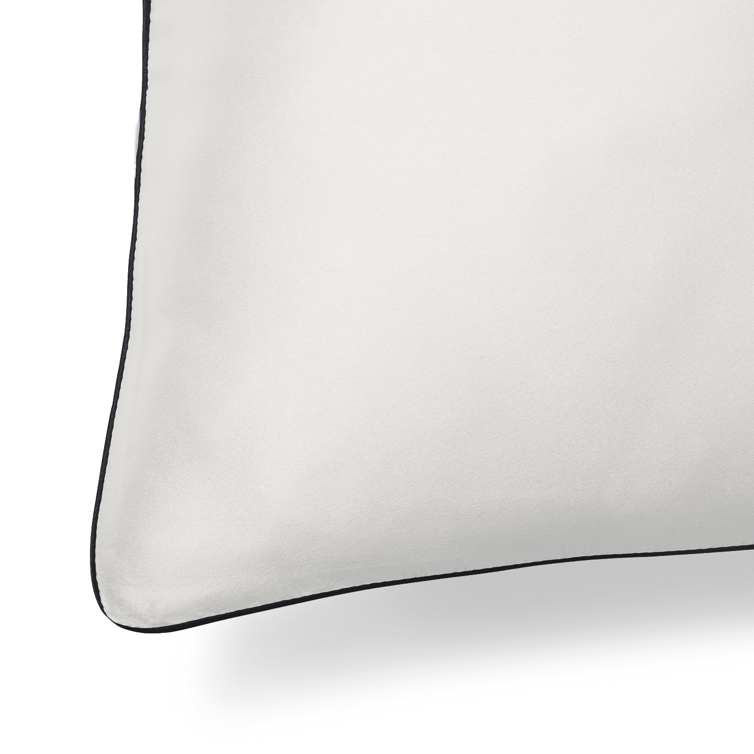 A close-up image of the Silk Pillowcase, showcasing its smooth white fabric with a dark border on one side. The pillowcase features a rounded corner, and the focus is on the texture and finish of the luxurious silk material, with the background in shadow.