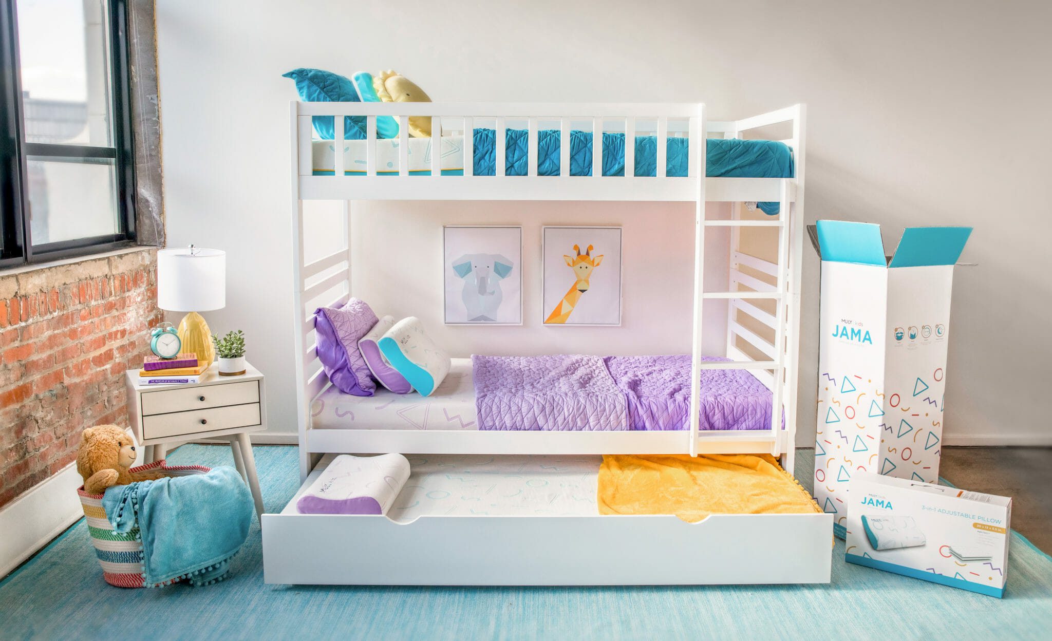 A neatly arranged children's bedroom with a white bunk bed, featuring the Mlily JAMA 5" Mattress. The top bunk is dressed in blue bedding and the bottom bunk in purple bedding. A drawer below the bed is partially pulled out. On the side, a nightstand holds a lamp, plant, and stuffed animals. A large box sits in the corner.