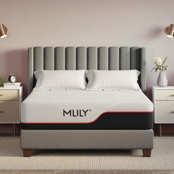 A neatly made bed with a grey upholstered headboard and a mattress labeled "Mlily Dream." The bed is flanked by two white bedside tables with drawers, each decorated with plants and vases. Two wall-mounted lights illuminate the setting, and a large plant is in the left corner.
