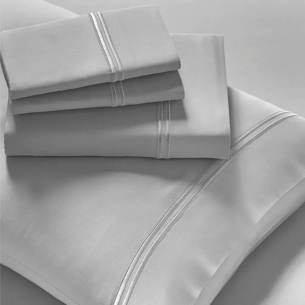 A neatly arranged stack of folded Refreshing TENCEL™ Lyocell Sheets - PureCare in grey, including two pillowcases, a flat sheet, and a fitted sheet. The linens feature a subtle, elegant stripe detail near the edges, enhancing their sleek, minimalist appearance.