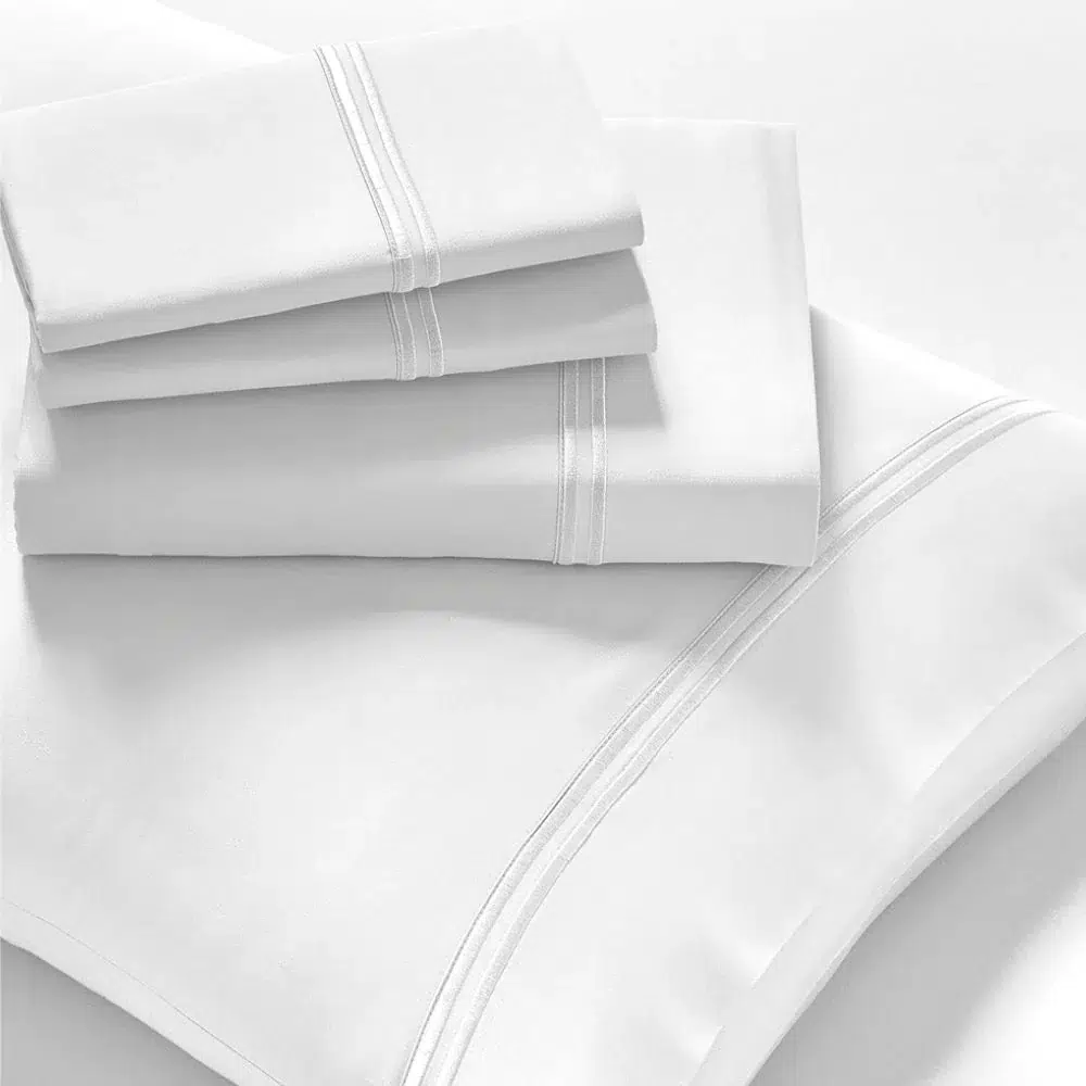 A neatly folded set of Refreshing TENCEL™ Lyocell Sheets from PureCare, including white bed sheets and pillowcases with subtle decorative stitching lines. The sheets are stacked on a white surface, showcasing their smooth texture and clean finish.