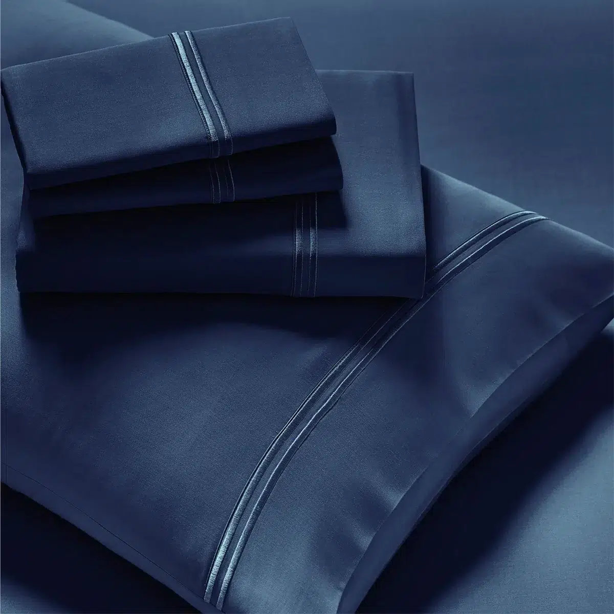 A neatly folded set of Refreshing TENCEL™ Lyocell Sheets - PureCare is shown. Four items are stacked, including pillowcases and flat sheets, each featuring a subtle, sleek striped design near the edges. The overall appearance is smooth and elegant.