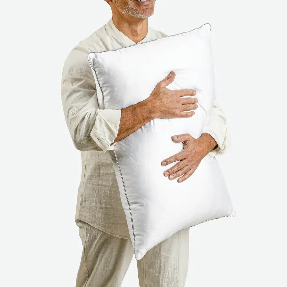 A person wearing light-colored sleepwear is holding a large Cooling Shattered Ice Pillow - PureCare close to their chest. The background is plain white, and the person is smiling.