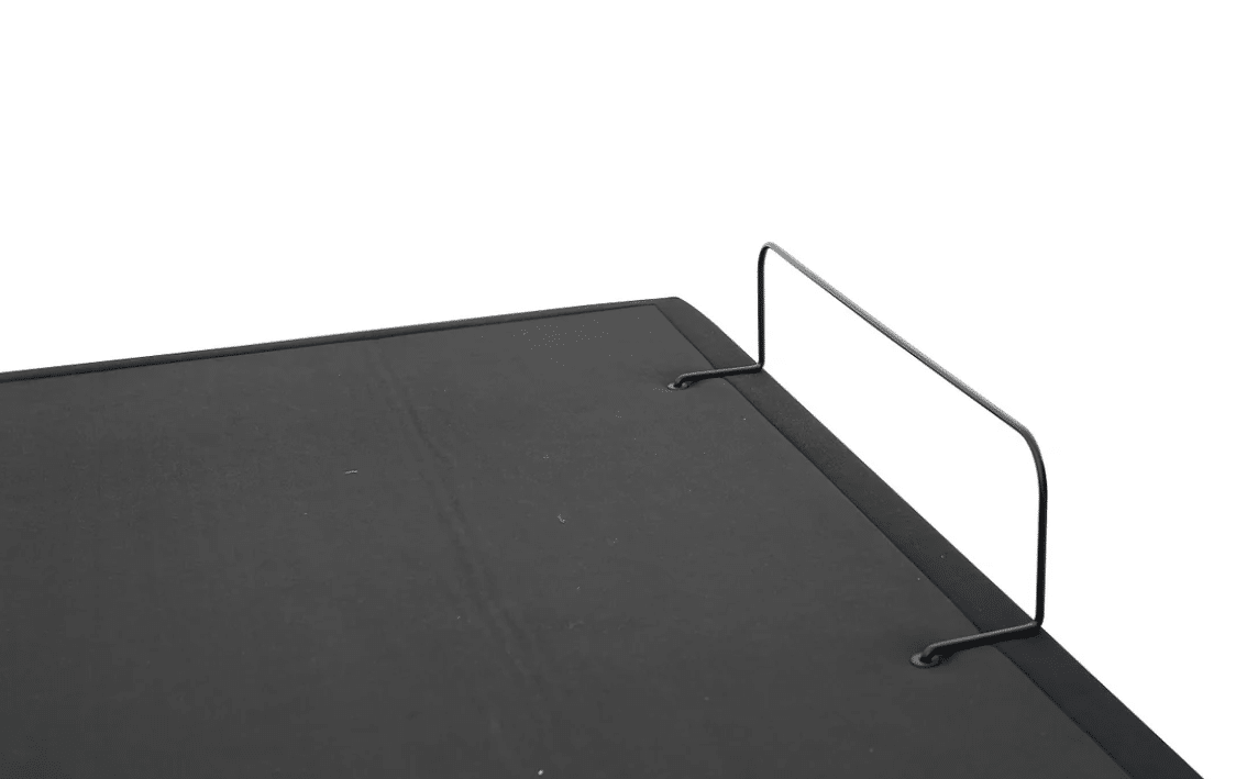 A close-up image of the black tabletop surface of the DUETTO Split Top Adjustable Base, featuring two metal wire brackets extending vertically from the edge for support or securing objects, set against a white background.