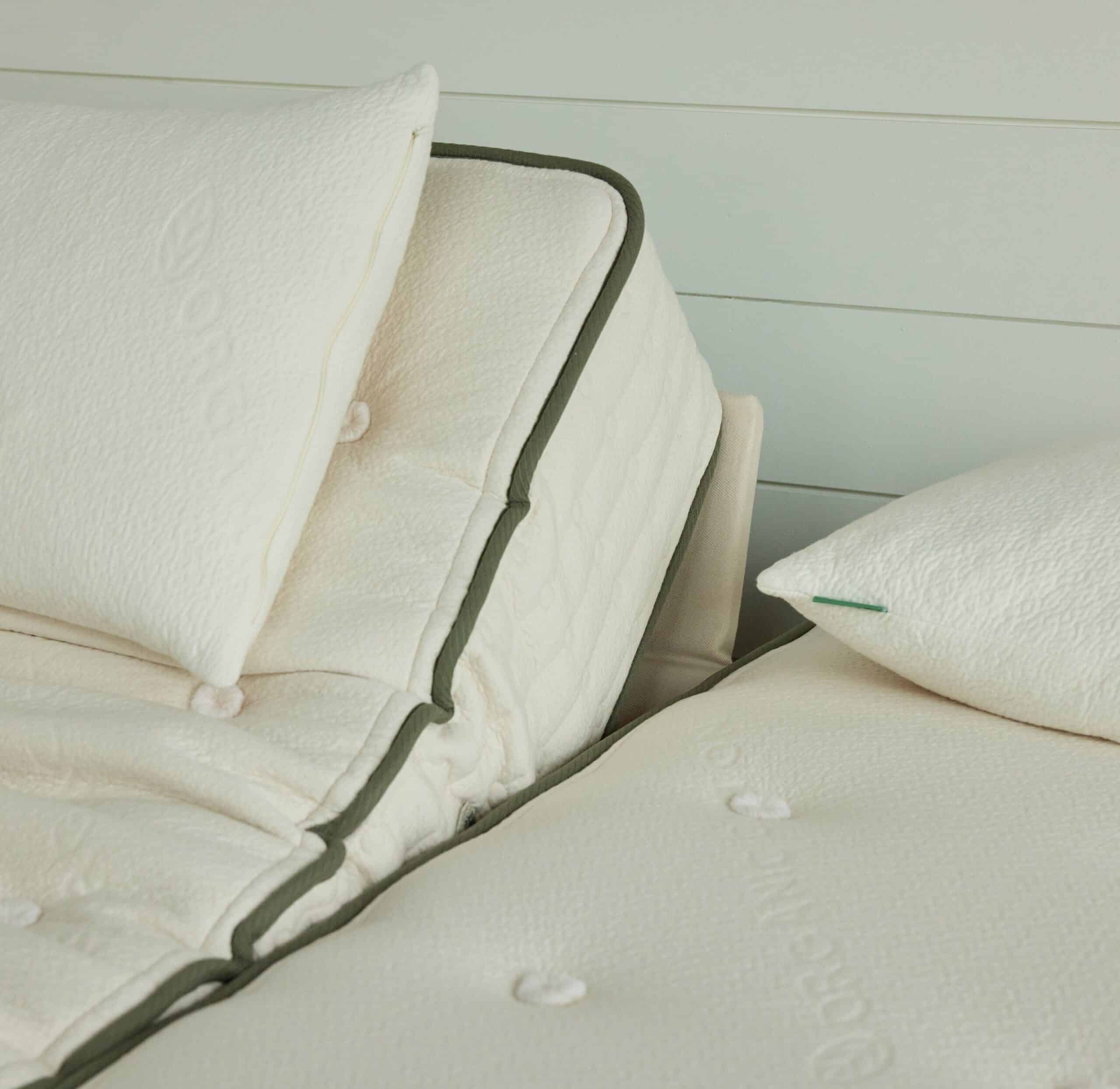 Close-up of adjustable twin beds with creamy white mattresses and pillows. One of the beds is raised at the head end, showcasing its adjustable feature. The mattresses have a textured surface with subtle patterns and green trimming along the edges.