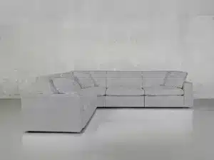 A modular L-shaped gray sectional sofa with cushioned seats and backs is placed in a minimalistic, light-gray room with a smooth floor and bare walls. The sofa appears comfortable and spacious, suitable for a modern living area.