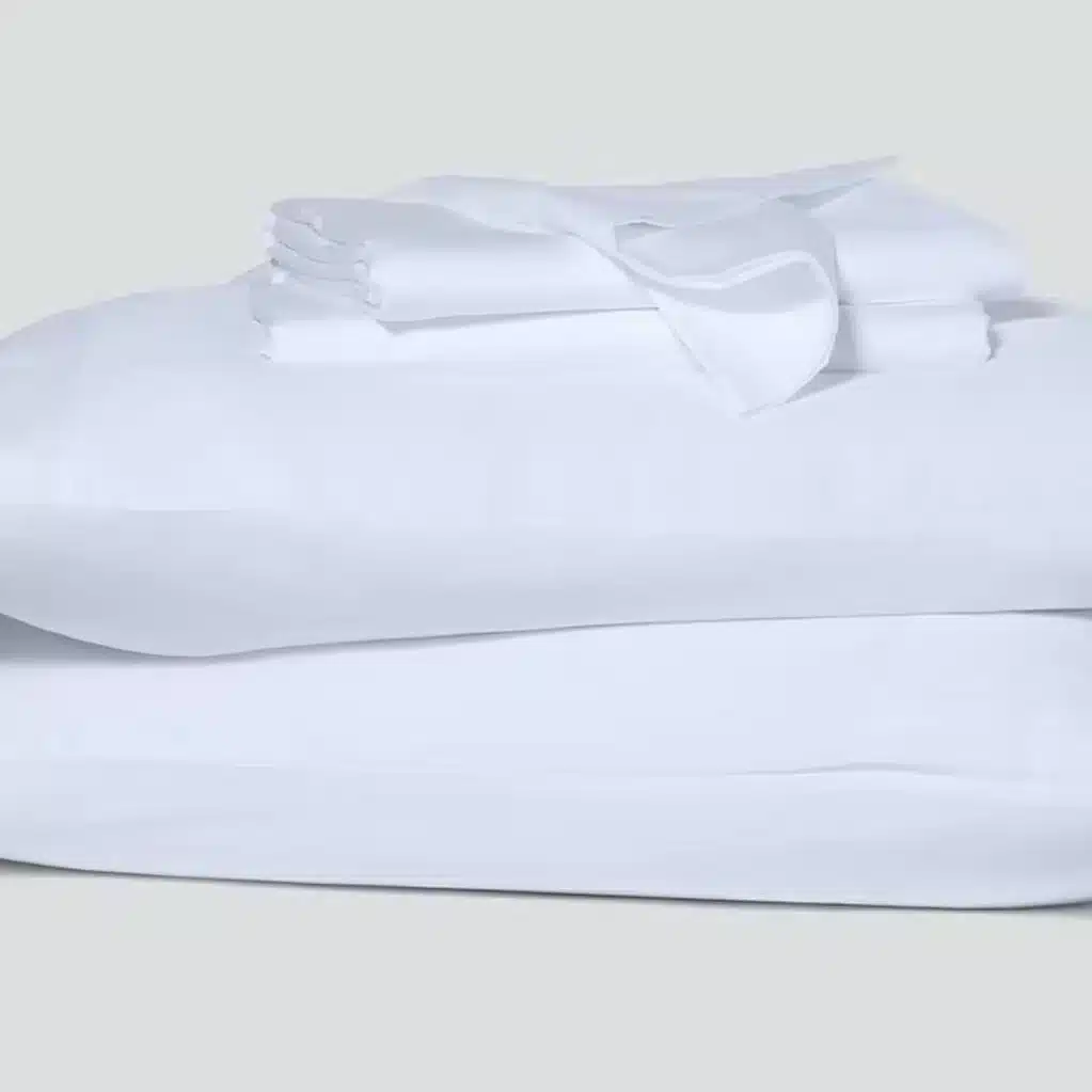 A neatly folded stack of white bed linens, including sheets and pillowcases, placed on a neutral background.
