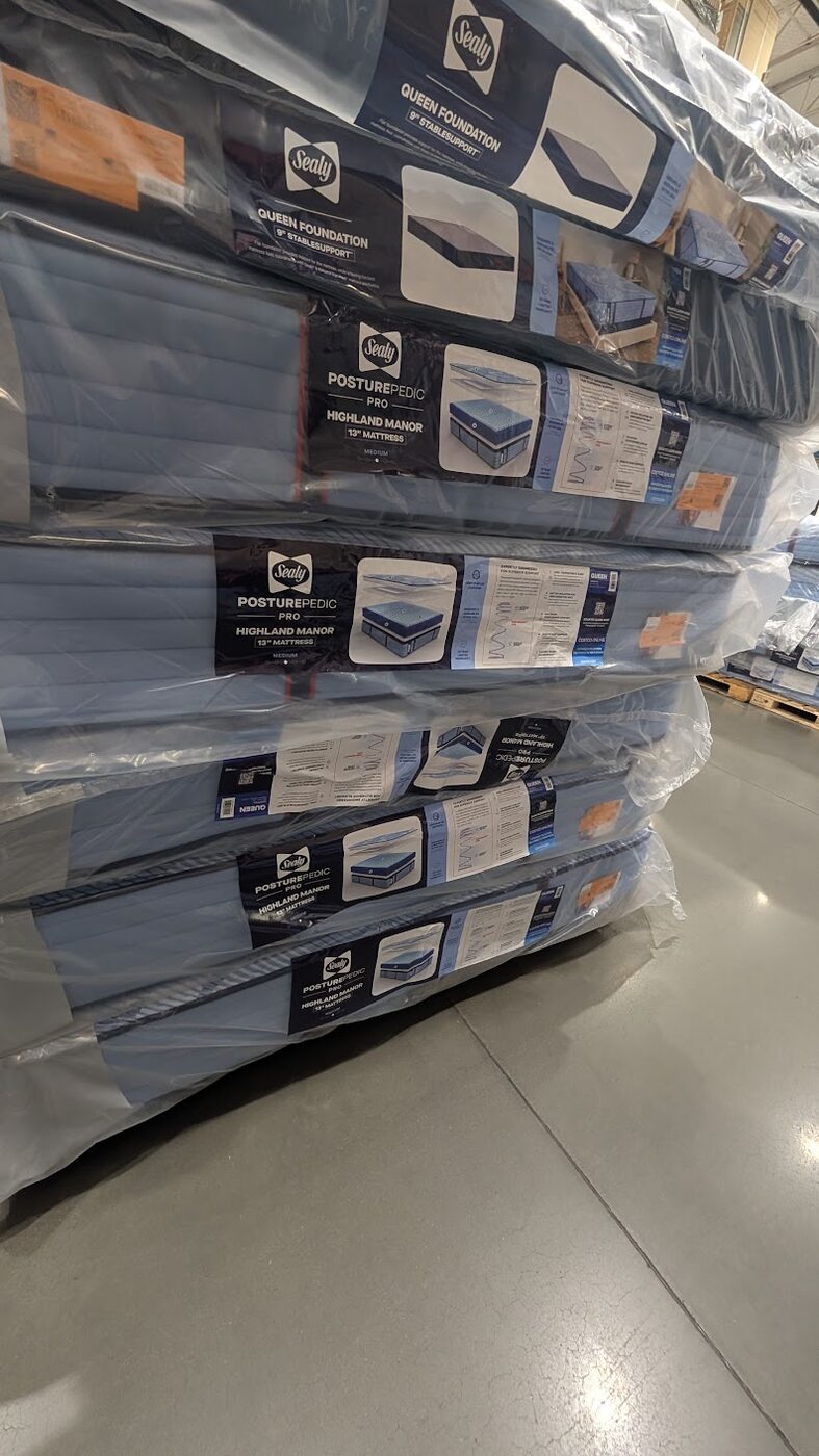Sealy Posturepedic Pro Highland Manor 13-inch queen mattress stacked on a pallet at Costco with the Sealy Queen Foundation on top